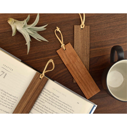 Three wood bookmarks with leather tassles against wooden backdrop.
