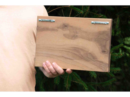 Person holding a wooden wall art with metal brackets against a natural background