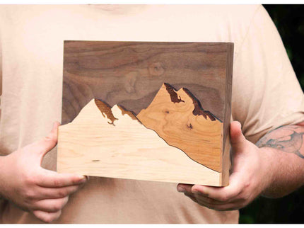 Person holding wooden wall art with mountain design
