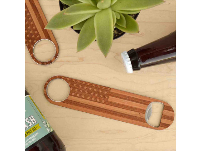 Wooden bottle opener with American flag design on a wooden surface with beer bottles and a plant.