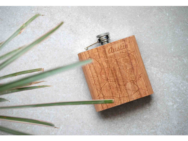 Wooden flask with engraved text on a light gray surface with green leaves.