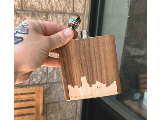 Wooden flask with laser-engraved design held by a hand against a brick wall.