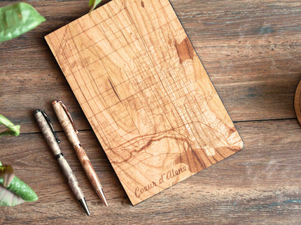 Wooden cutting board with engraved text on a wooden surface with a pen and leaves.
