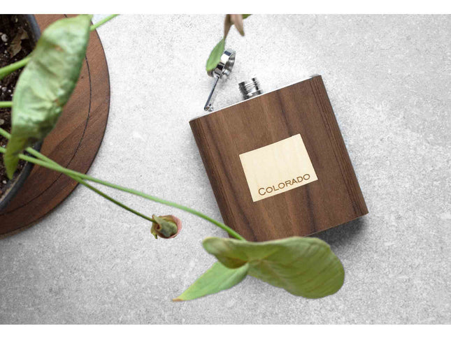 Wooden flask with 'Colorado' inlay on a gray surface with a plant in the corner.