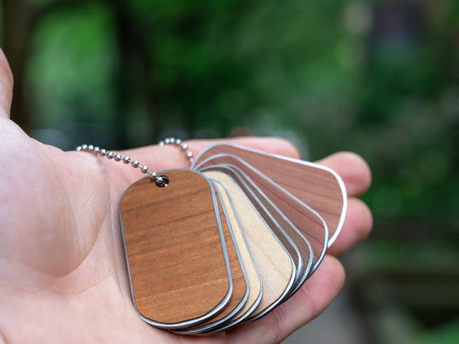 A hand holding multiple custom dog tags with wood and stainless steel components, in various shades and colors.