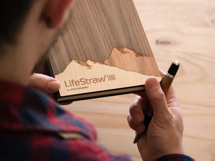 Person holding a wood pen and wooden mountain journal engraved with LifeStraw logo