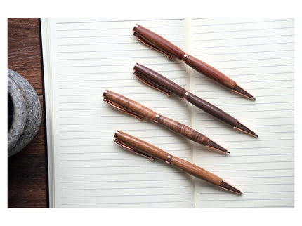Four brown pens on a sheet of lined paper with a wooden desk and stone object in the background.