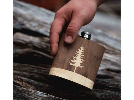 Wooden flask with tree engraving held by a hand on a rustic wooden surface