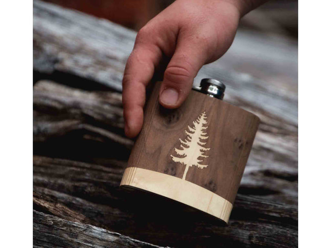 Wooden flask with tree engraving held by a hand on a rustic wooden surface