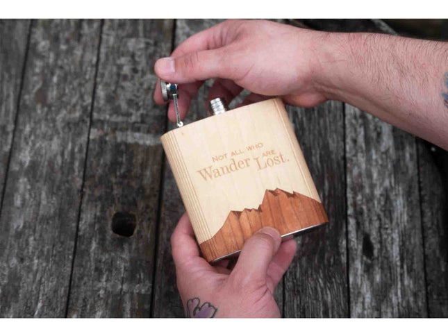 Wooden flask with engraved text held by a person against a wooden background