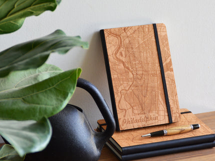 Wooden notebook with map design and pen on a wooden surface with a plant in the background
