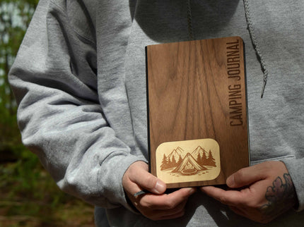 Person holding a wooden camping journal with nature-themed design