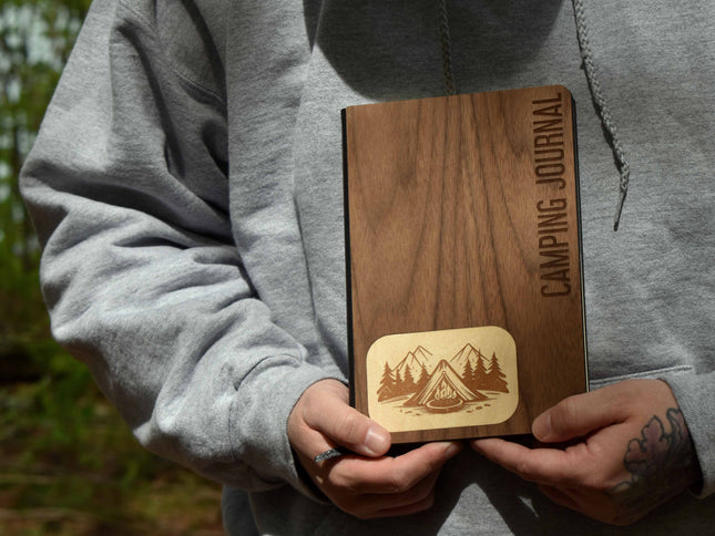 Person holding a wooden camping journal with nature-themed design