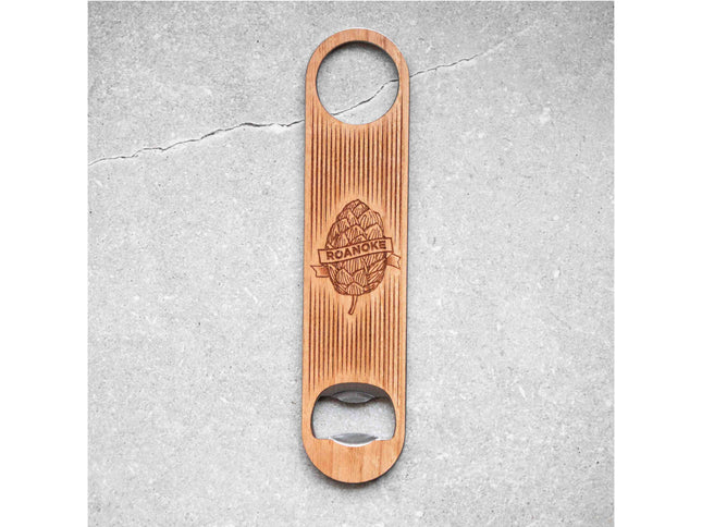 Wooden bottle opener with engraved design on a gray concrete surface