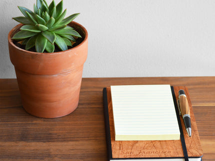 Notebook with pen and potted plant on a wooden surface