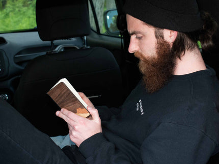 Man with a beard in the back of a Jeep Renegade, writing in his wooden mountain journal.