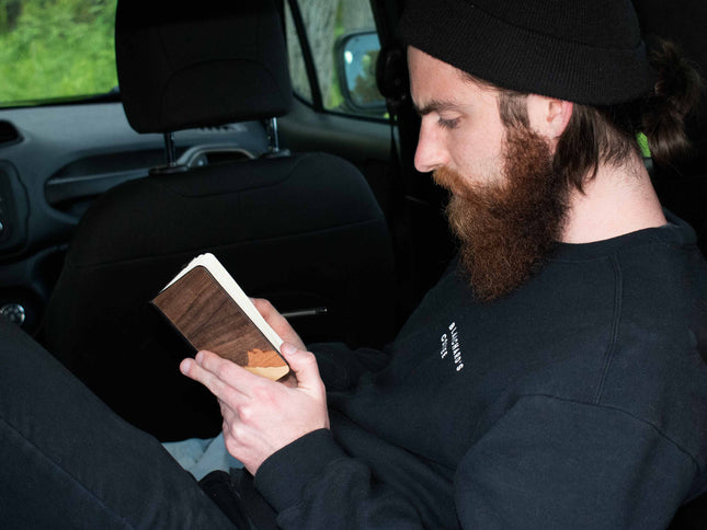 Man with a beard in the back of a Jeep Renegade, writing in his wooden mountain journal.