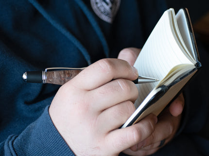 Person holding a notebook and pen, wearing a dark blue jacket with a logo.