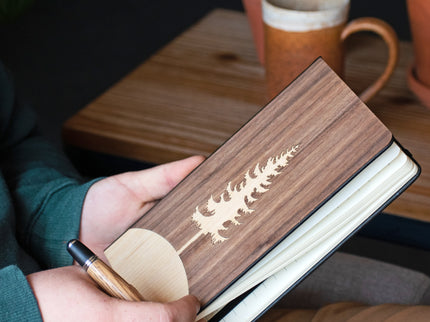 Wooden notebook with laser cut design held by a person, with a blurred background of a table and mug.