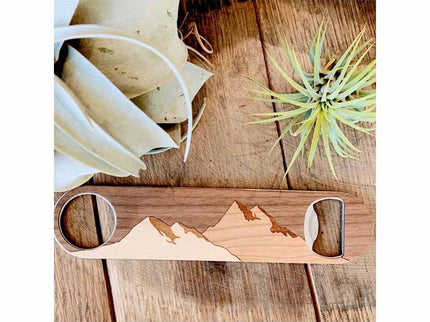 Wooden drink coaster with mountain design on a wooden surface with plants.