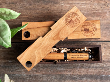 Two wooden pen boxes photographed against a dark wood background, both engraved with the Department of the Interior logo.