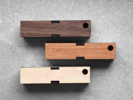 Three Handcrafted Wooden Pen Boxes lying on a grey surface, showcasing different wood finishes.