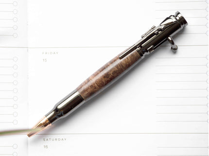 A handcrafted wooden bolt action ballpoint pen lying on paper, with metal accents and a mechanism visible.