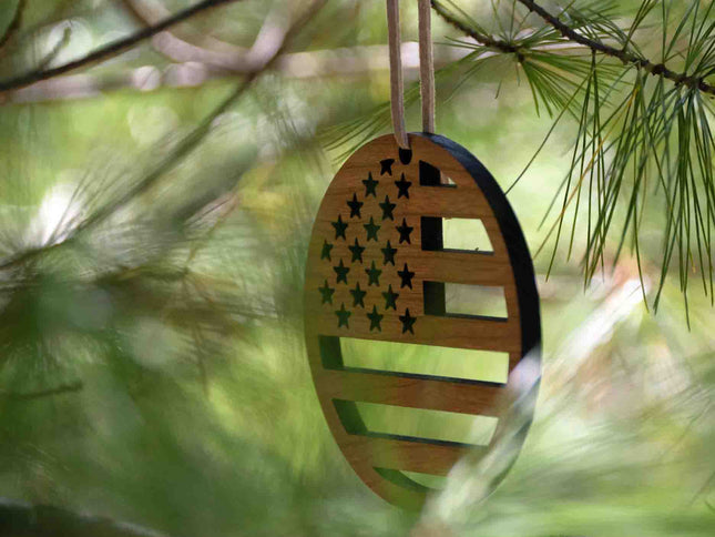 An image of a cherry wood and leather christmas ornament with the American Flag design by Autumn Woods Co carved into it