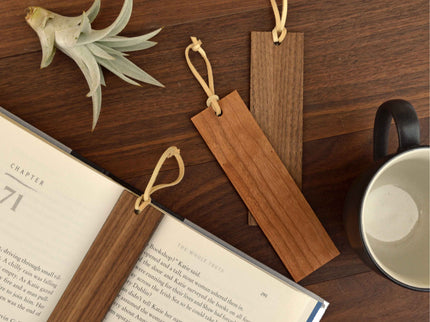 Three wood bookmarks with leather tassles against wooden backdrop.