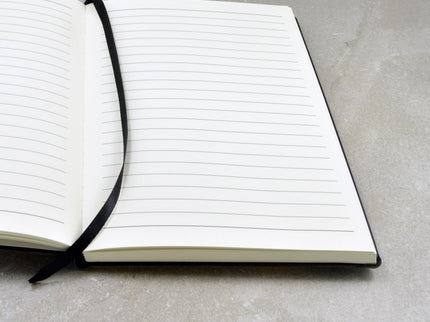 Lined paper page notebook with black ribbon bookmark on stone counter.